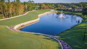 A golf course with a pond, a stone wall, and a fountain.
