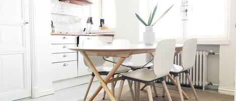 A modern kitchen with white cabinetry, wooden shelves, and a dining area with a table and chairs.