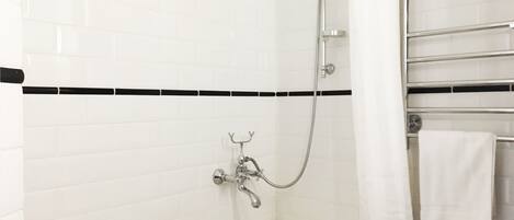 A bathroom with a white bathtub, a shower with a handheld showerhead, and a towel rack with a white towel.