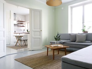 A modern living room with a grey sofa, a wooden coffee table, and a kitchen visible through an open door. - Roost Kruunuhaka (Helsinki)