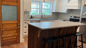 A modern kitchen with a wooden island, bar stools, and a ceiling fan. - 4 Bed 3.5 Bath Pool Mid Island, Quiet Garden lined Street, steps from the Beach! (Ocean Isle Beach)
