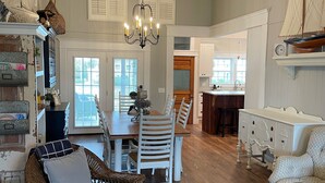 A spacious living room with a dining area, wooden floors, and a chandelier. - 4 Bed 3.5 Bath Pool Mid Island, Quiet Garden lined Street, steps from the Beach! (Ocean Isle Beach)