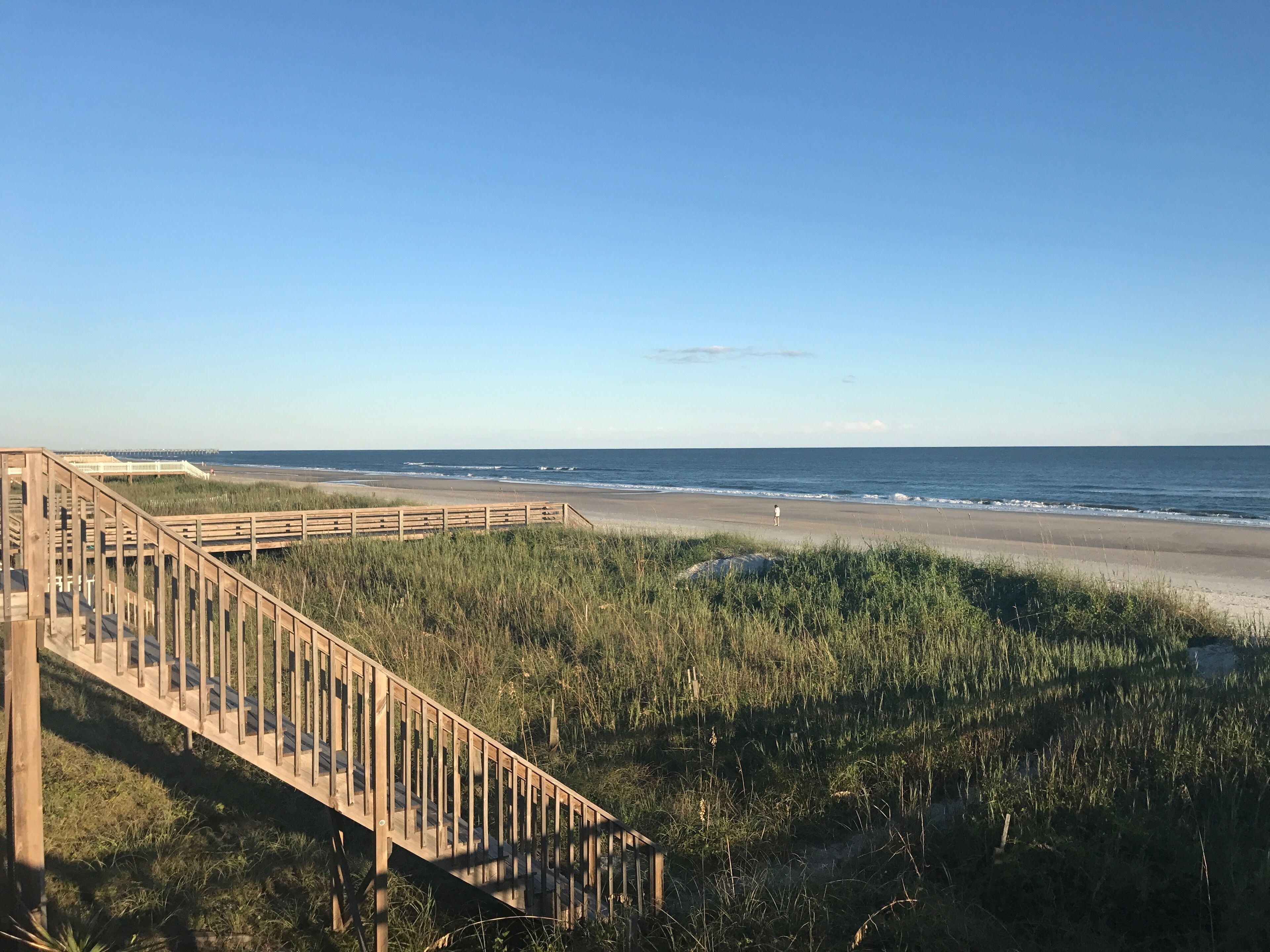 A wooden boardwalk leading to a beach with a clear view of the ocean.