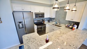 A modern kitchen with white cabinets, stainless steel appliances, granite countertops, and pendant lighting. - Destin West Gulfside #603 ~WOW! ~Spectacular Penthouse View! ~Free Beach Service (Fort Walton Beach)