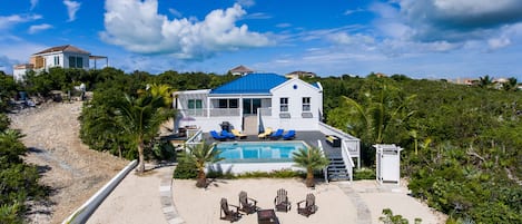 Una casa grande con piscina, rodeada de exuberante vegetación y una playa de arena.