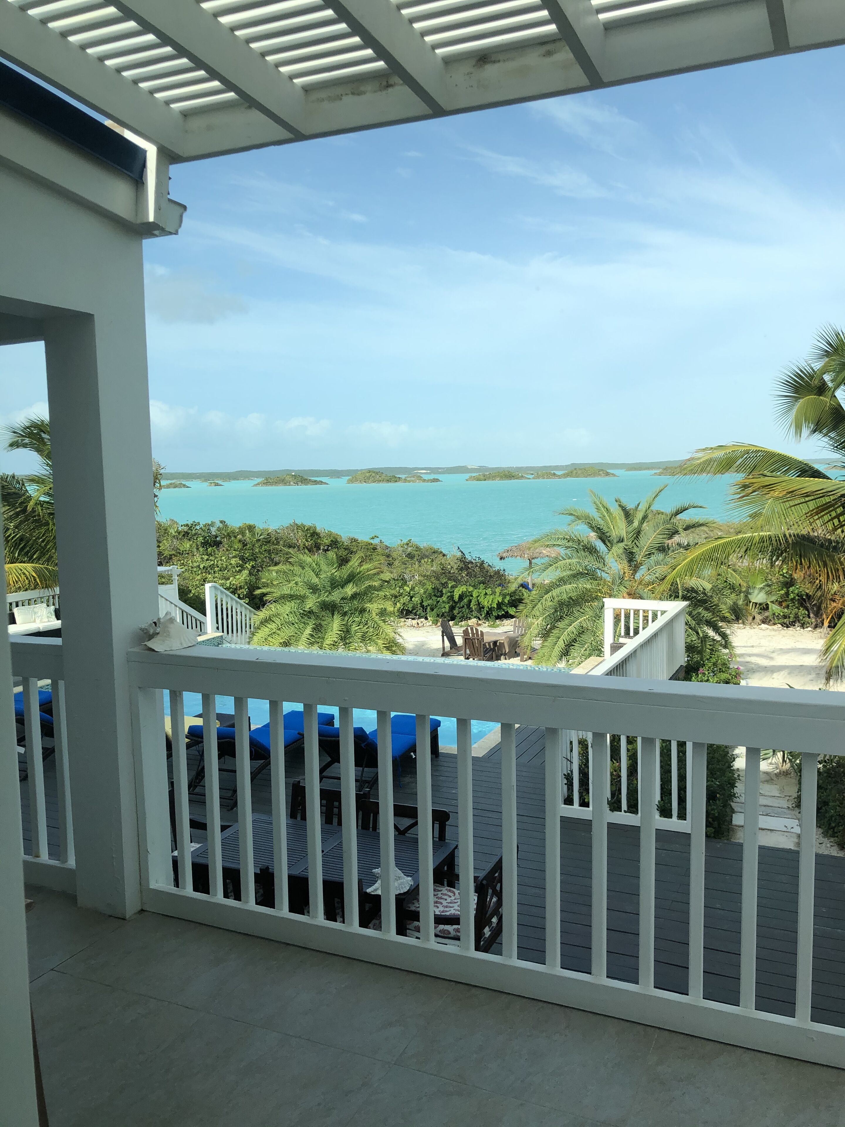 A balcony with a view of a turquoise sea and palm trees.