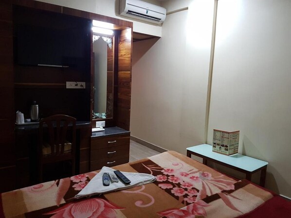 Un dormitorio con cama, escritorio, silla, cómoda, espejo y aire acondicionado.