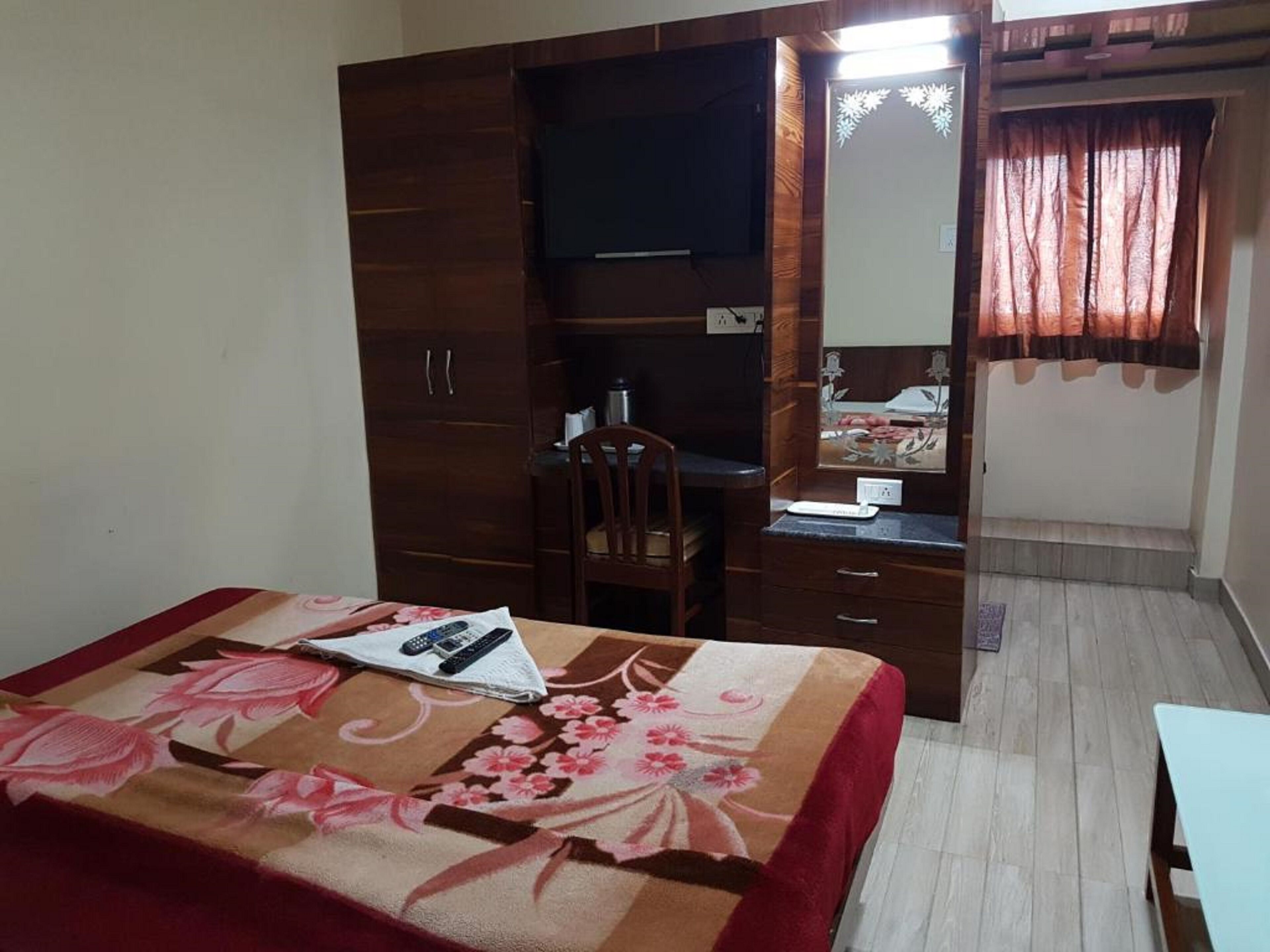 A bedroom with a bed, a desk, a chair, a wardrobe, a mirror, and a window with curtains.
