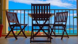 A balcony with two wooden chairs and a small table, overlooking a scenic ocean view.