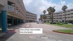 Fila de condominios con vista al mar, balcones, coches aparcados y palmeras.