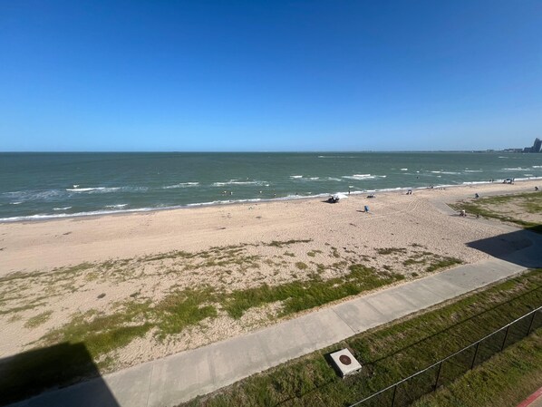 Una playa con un paseo marítimo de hormigón, zonas verdes y el océano.