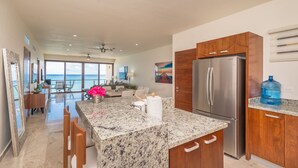 A spacious kitchen with a large island, stainless steel refrigerator, and wooden cabinets. - Luxury Penthouse Beachfront Condo with Private Rooftop (Akumal)