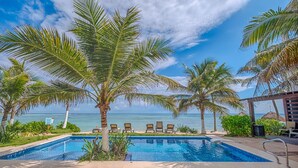 A pool area with a view of the ocean, surrounded by palm trees and lounge chairs. - Luxury Penthouse Beachfront Condo with Private Rooftop (Akumal)