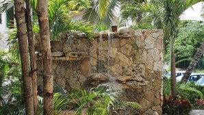 A stone waterfall structure surrounded by tropical plants. - Luxury Penthouse Beachfront Condo with Private Rooftop (Akumal)