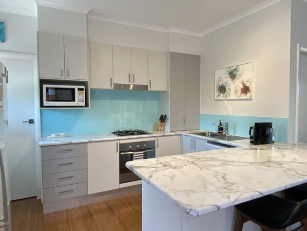 Una cocina moderna con gabinetes blancos, microondas integrado, estufa a gas y encimera de mármol.