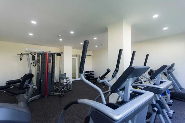 Une salle de sport équipée de divers appareils d’exercice, notamment des tapis de course, une machine de musculation et des haltères.