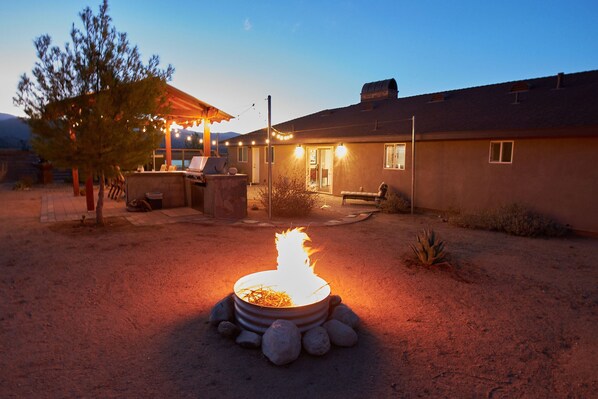 Ein Garten mit Feuerstelle, Gartenmöbeln und einer überdachten Terrasse.