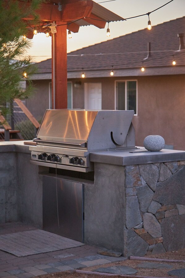Une cuisine extérieure dotée d’un barbecue encastré, d’un plan de travail en pierre et d’une sphère décorative en pierre.