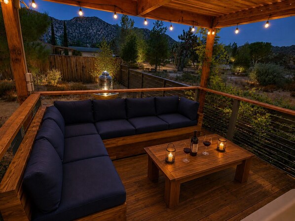 An outdoor seating area with a wooden deck, a dark-colored sofa, and a wooden table with candles and wine glasses.