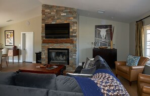 Ein Wohnzimmer mit Kamin aus Stein, einer Couch, einem Couchtisch und einem an der Wand befestigten Fernseher.