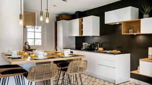 Une cuisine moderne avec des meubles blancs, une table à manger en bois, des chaises en osier et un pare-feu noir.