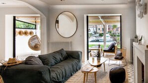 Un salon moderne avec un canapé gris foncé, un miroir rond et une vue sur les bateaux à travers de grandes fenêtres.