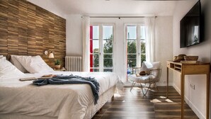 Une chambre à coucher avec une tête de lit en bois, un lit avec du linge de maison blanc, un bureau avec une chaise et un téléviseur fixé au mur.
