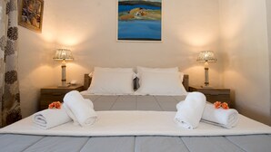 A hotel room with a large bed, two bedside tables with lamps, a painting on the wall, and towels on the bed. - The Veranda of Gavrion - Premium Cycladic House (Andros)