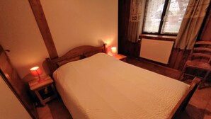 Une chambre à coucher avec un lit, une table de chevet, une lampe, une chaise et une fenêtre avec des rideaux.