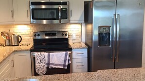 A modern kitchen with white cabinets, a stainless steel oven, a microwave, and a refrigerator.