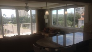 A spacious living area with a large window, a ceiling fan, and a dining table with chairs.