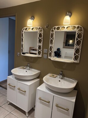 A bathroom with two white sinks, each with a mirror above. There are two wall-mounted light fixtures above the mirrors. - Charming air-conditioned cottage "the cabin" and its private and independent garden (Sommières)