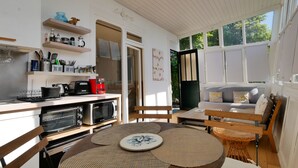 A kitchen with a microwave, toaster, and coffee maker. There is a dining table with placemats and a chair. A window provides natural light.
