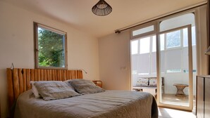 A bedroom with a wooden headboard, a large bed with a beige quilt, a bedside table, and a view of the outdoors through a sliding glass door.