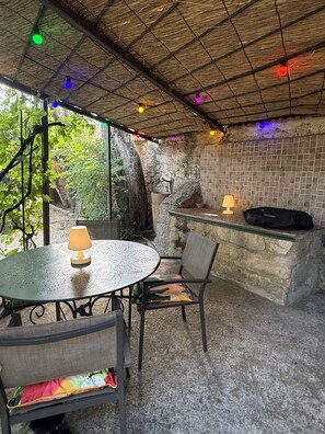 Un patio al aire libre con una mesa redonda, sillas, una lámpara y una parrilla.