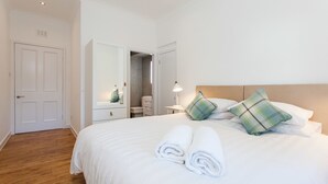 A neatly made bed with rolled towels, a wooden headboard, and two plaid pillows. - The Old Manse House - Apartment (Ayr)