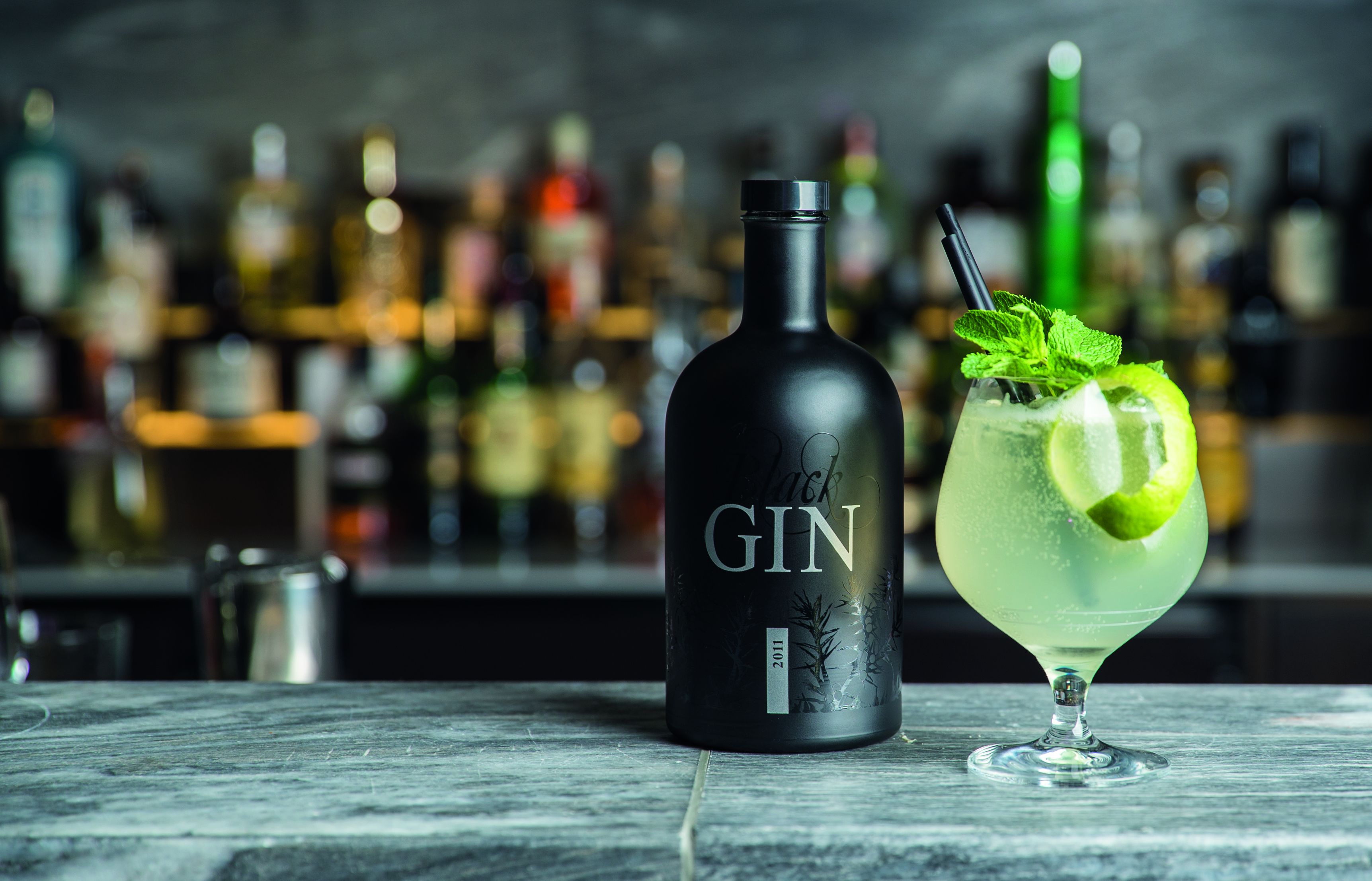 Una botella de ginebra y un cóctel sobre una barra, con un fondo desenfocado de diversas botellas.