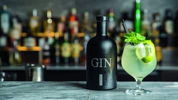 Una botella de ginebra y un cóctel sobre una barra, con un fondo desenfocado de diversas botellas.