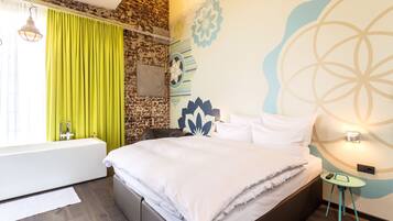 A modern bedroom with a large bed, a small bedside table, a green curtain, a wall-mounted light, and a decorative wall piece.