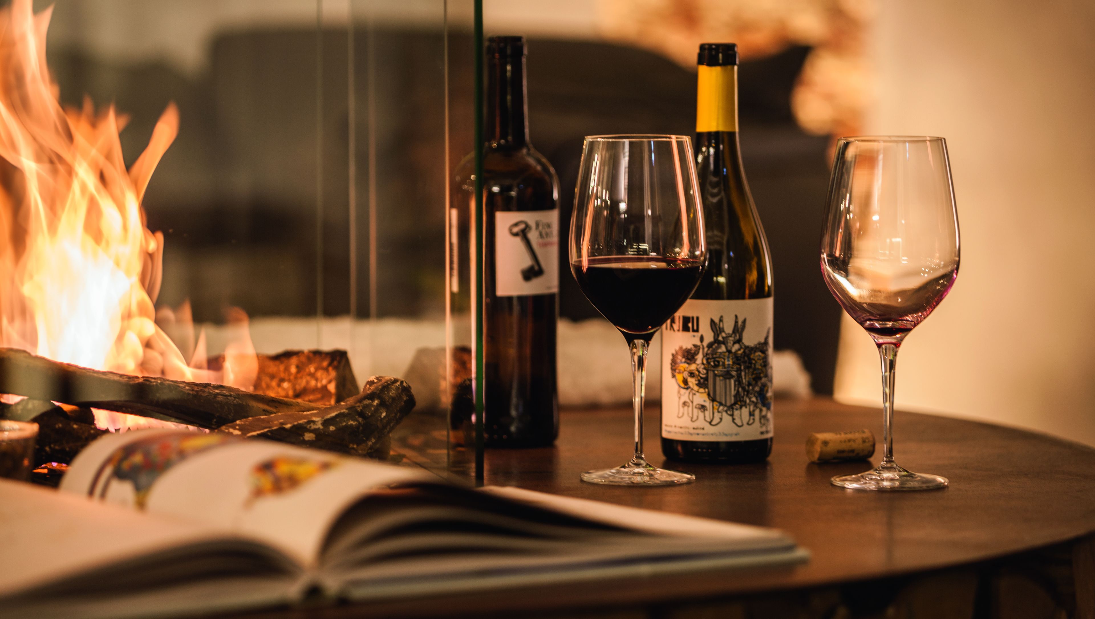 Una mesa con un libro, dos copas de vino y dos botellas de vino.