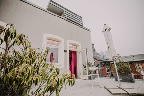 Un edificio moderno con fachada blanca, un balcón con barandilla y una puerta con cortina rosa.