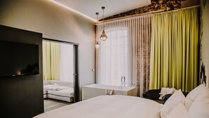 A hotel room with a large bed, a flat-screen TV, a sofa, a bathroom with a sink and mirror, and a window with curtains. - Hotel & Restaurant heyligenstaedt (Giessen)