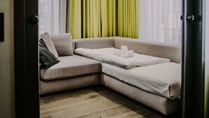 A room with a sectional sofa, a bed, and a large window with sheer curtains. - Hotel & Restaurant heyligenstaedt (Giessen)