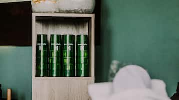 A bathroom with a wooden shelf holding green bottles and a white towel on a counter.