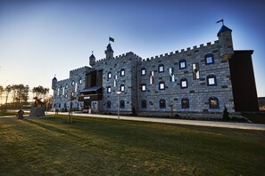 A castle-like building with multiple towers and arched windows, surrounded by a well-maintained lawn and pathway. - LEGOLAND Castle Hotel DENMARK (Billund)
