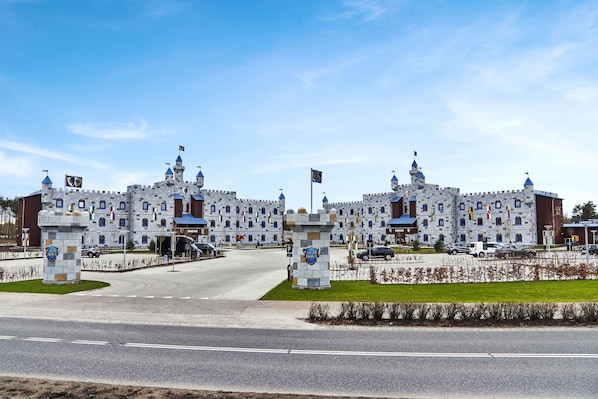 A castle-like building with multiple towers and flags, a parking area, and a road in front. - LEGOLAND Castle Hotel DENMARK (Billund)