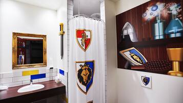Une salle de bain avec un miroir, un lavabo et un rideau de douche orné d’un emblème représentant la tête d’un lion.