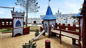 Une aire de jeux sur le thème du château, avec un toboggan et des bancs en bois.