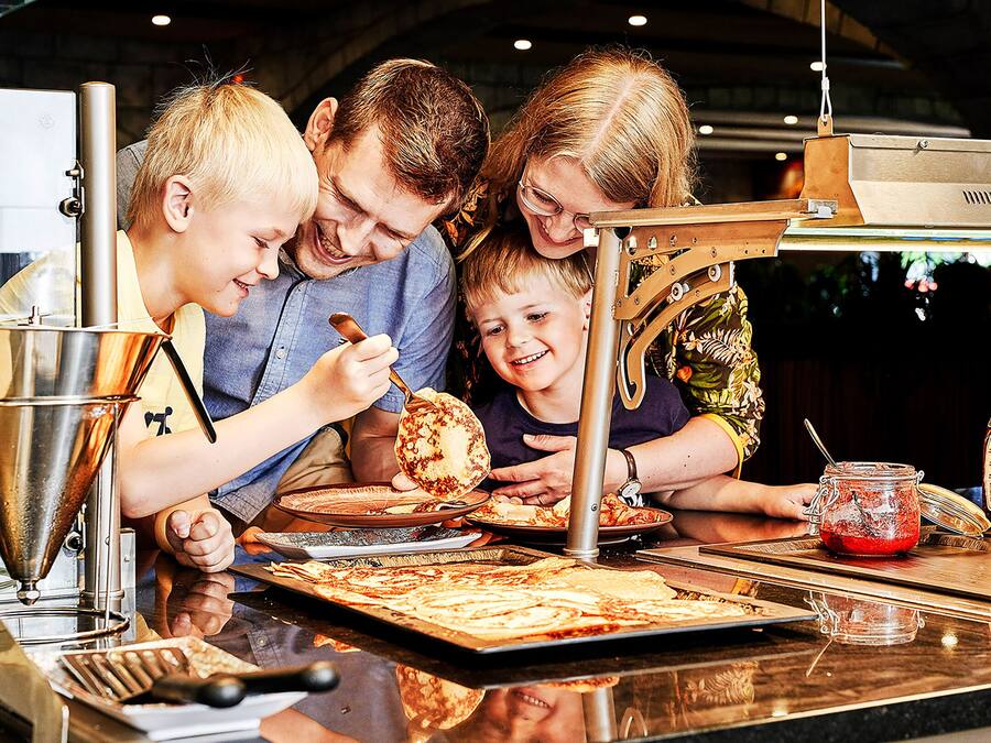 Eine Familie bereitet Essen an einer Arbeitsfläche mit verschiedenen Küchenutensilien und Zutaten zu.