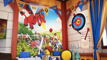 Una habitación con un mural de temática medieval, banderines y una diana en la pared.